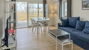 A modern living room with a sofa, a dining table with chairs, a small table, and a bookshelf.