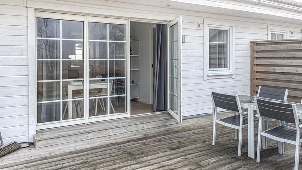 A wooden deck with a table and chairs, a sliding glass door leading to an interior space, and a small window on the side.