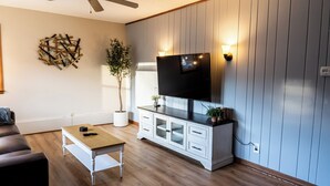 Een woonkamer met een plafondventilator, een flatscreen televisie bevestigd aan een witte kast, een houten salontafel en een potplant.