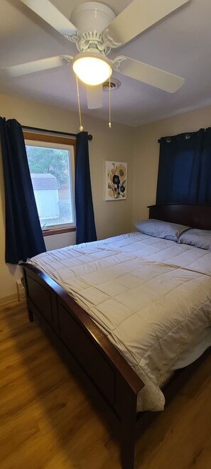 Un dormitorio con cama, ventilador de techo, ventana con cortinas y una obra de arte colgada en la pared.
