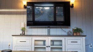 Een flatscreen televisie bevestigd aan een muur met twee wandlampen, een houten kastje eronder, en een potplant aan de rechterkant.