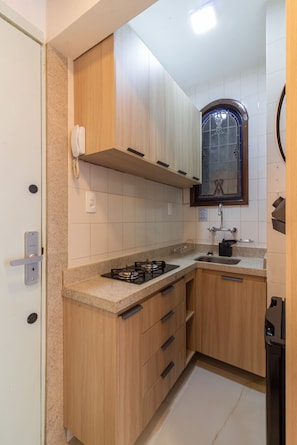 Een kleine keuken met houten kastjes, een gasfornuis, een spoelbak en een raam met decoratief glas.