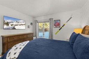 A bedroom with a bed, a dresser, a ski-themed painting, a ski pole, and a window with a view of mountains.
