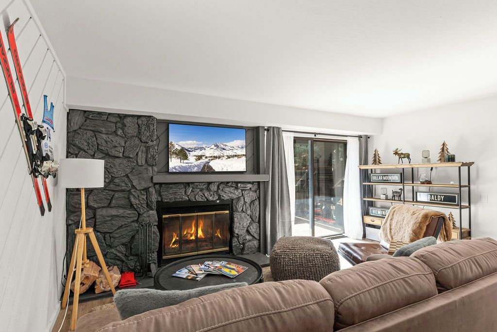 A living room with a stone fireplace, a television, a sofa, and a bookshelf.
