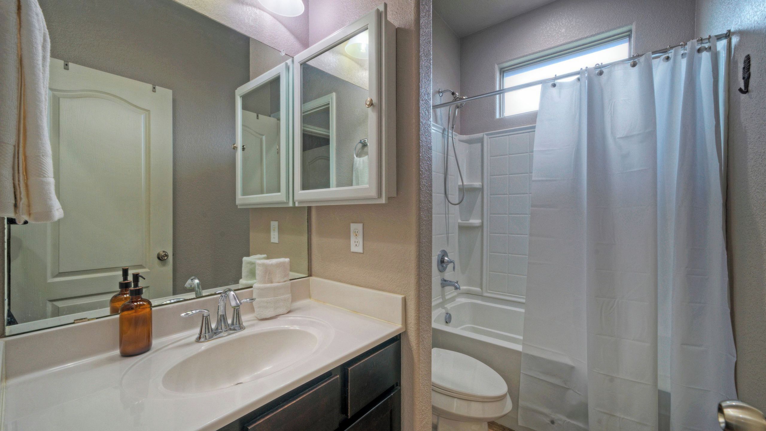 A bathroom with a sink, mirror, and shower.