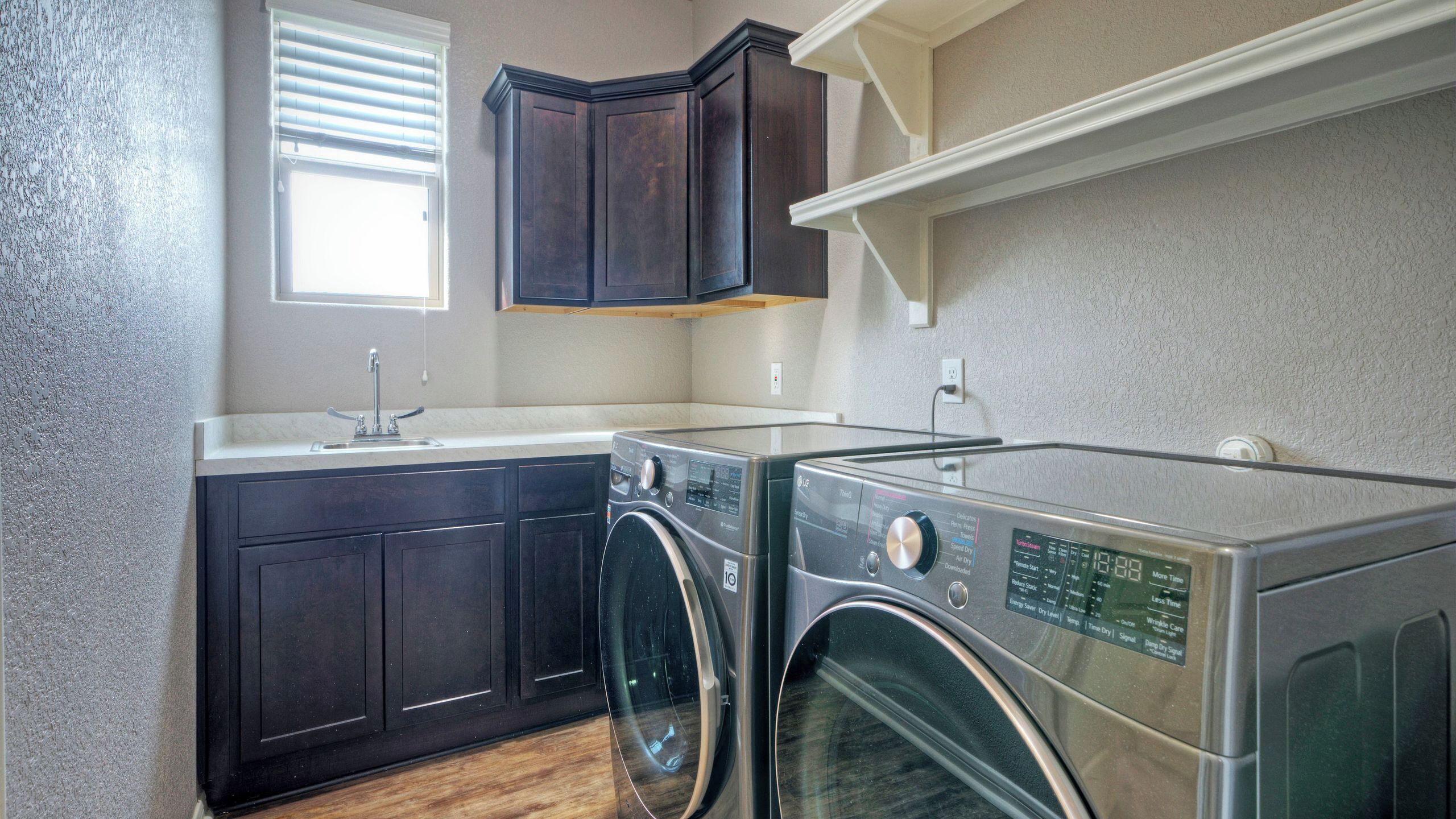 A laundry area with a washing machine and dryer, dark wooden cabinets, a window with blinds, and a white countertop.
