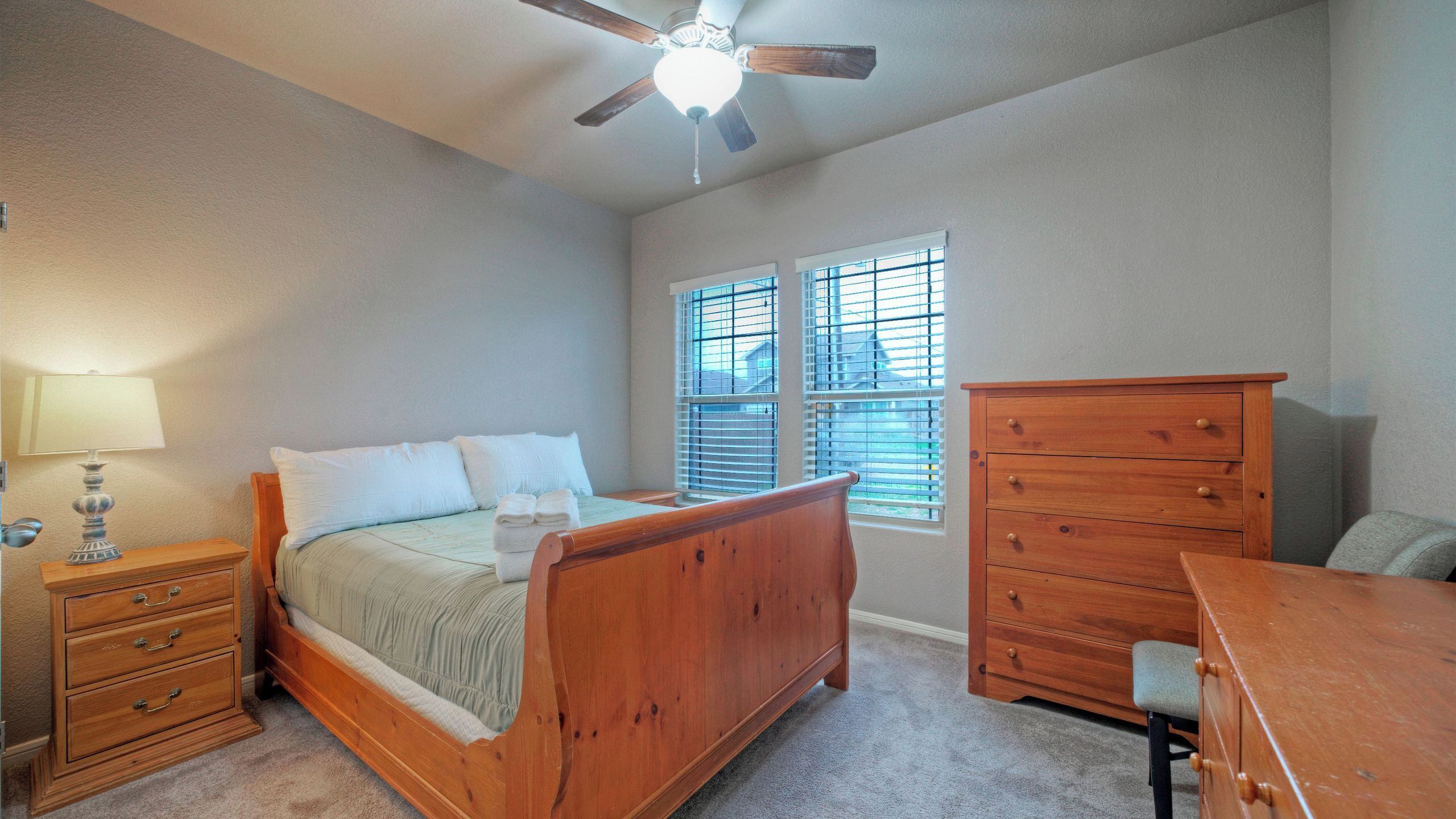 A bedroom with a bed, a dresser, a nightstand, a lamp, and a ceiling fan.