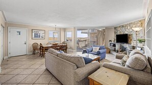 Ein geräumiger Wohnbereich mit Sofa, Couchtisch und Fernseher. Es gibt einen Essbereich mit Stühlen und Tisch. Der Raum verfügt über einen Balkon mit Aussicht.