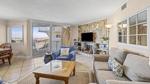 Ein Wohnzimmer mit Sofa, Sessel, Couchtisch, Fernseher und einem Balkon mit Blick.