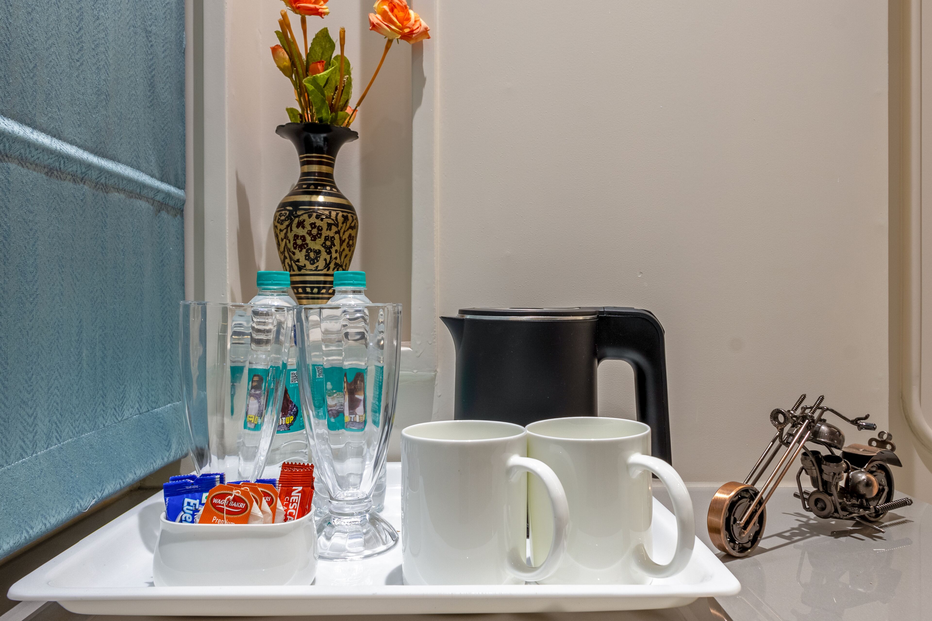 A tray with water bottles, a vase with flowers, a coffee maker, and a motorcycle model.