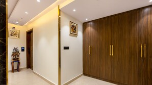 Een hal met een marmeren vloer, een houten garderobe met gouden handgrepen, een kunstwerk in een lijst aan de muur en een tafeltje met een plant.