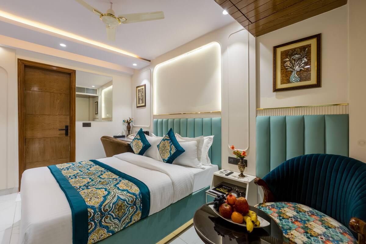 A modern hotel room with a bed, a seating area, a dining table with fruit, and a ceiling fan.