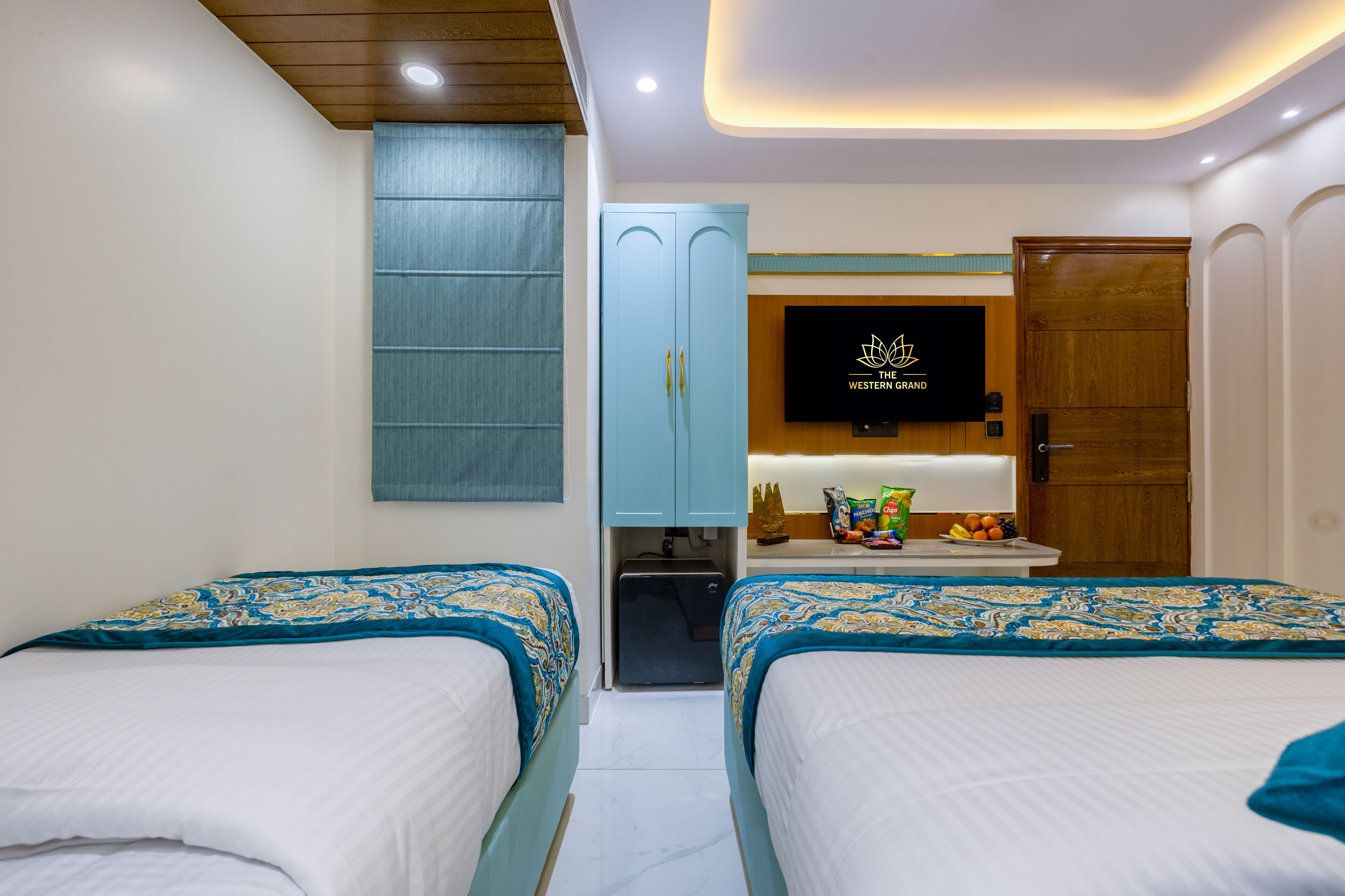 Habitación de hotel con dos camas, un armario, un televisor y una mesita con aperitivos.