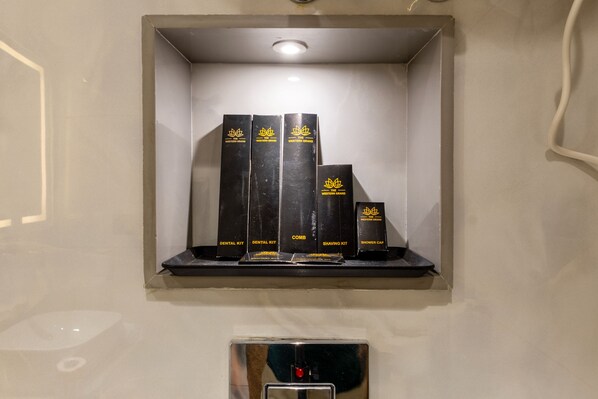 A shelf with black boxes labeled 'Western Grand' containing items like dental kits, combs, shaving kits, and shower caps. - The Western Grand (New Delhi)