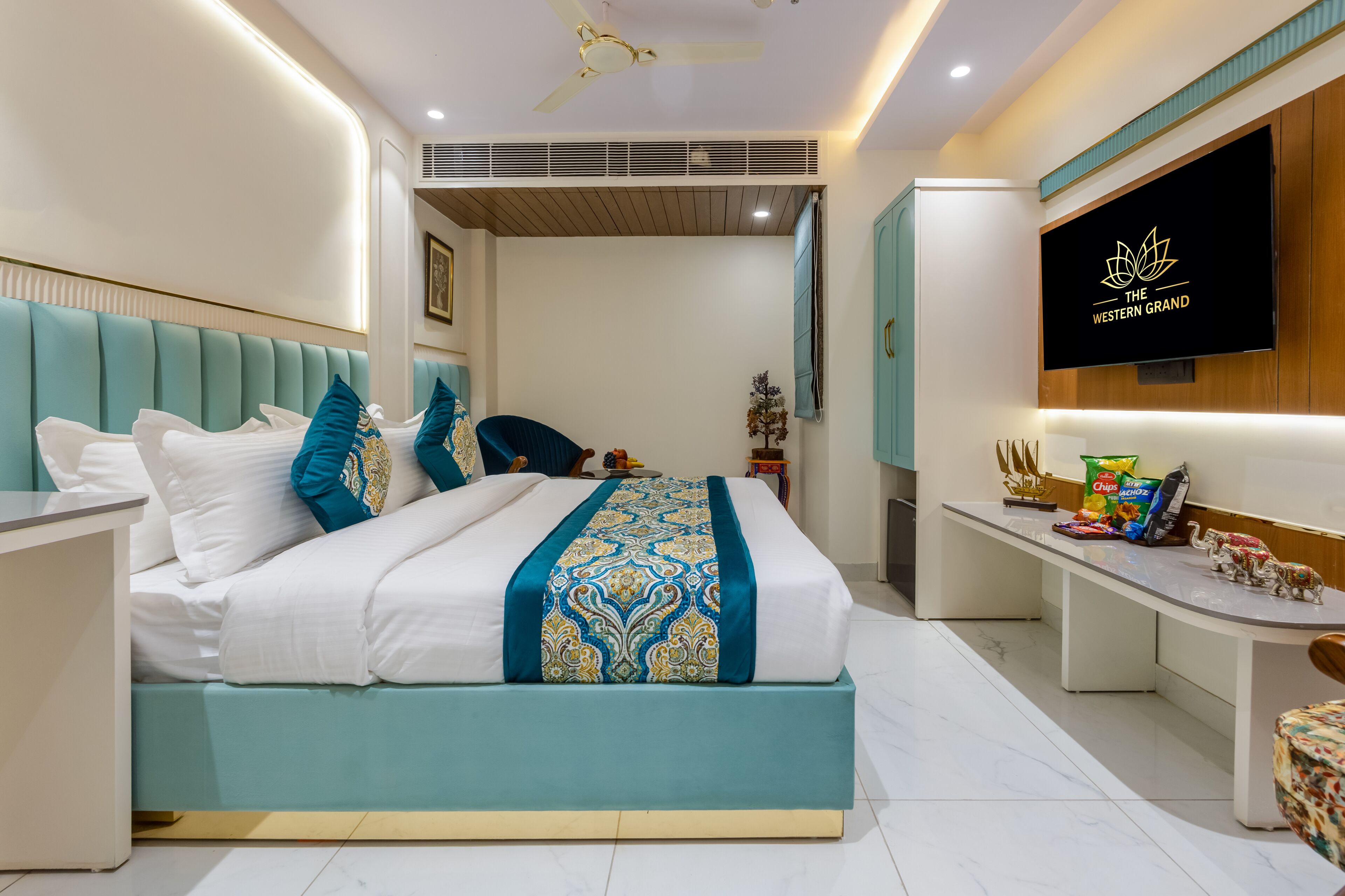 A modern hotel room with a bed, a desk, a TV, and a ceiling fan.