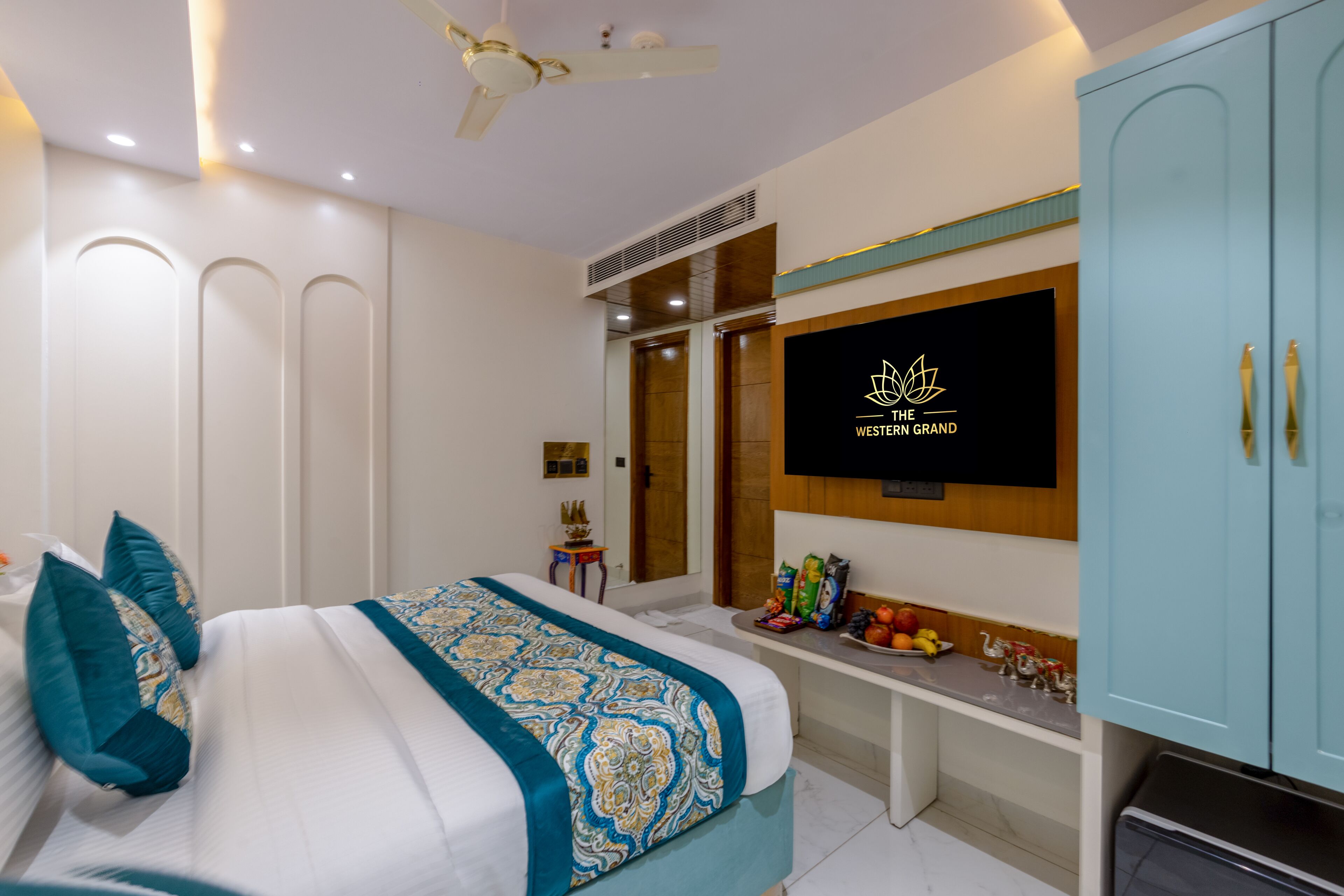 Ein modernes Hotelzimmer mit einem Bett, einem an der Wand montierten Fernseher, einem Deckenventilator und einem Kleiderschrank.