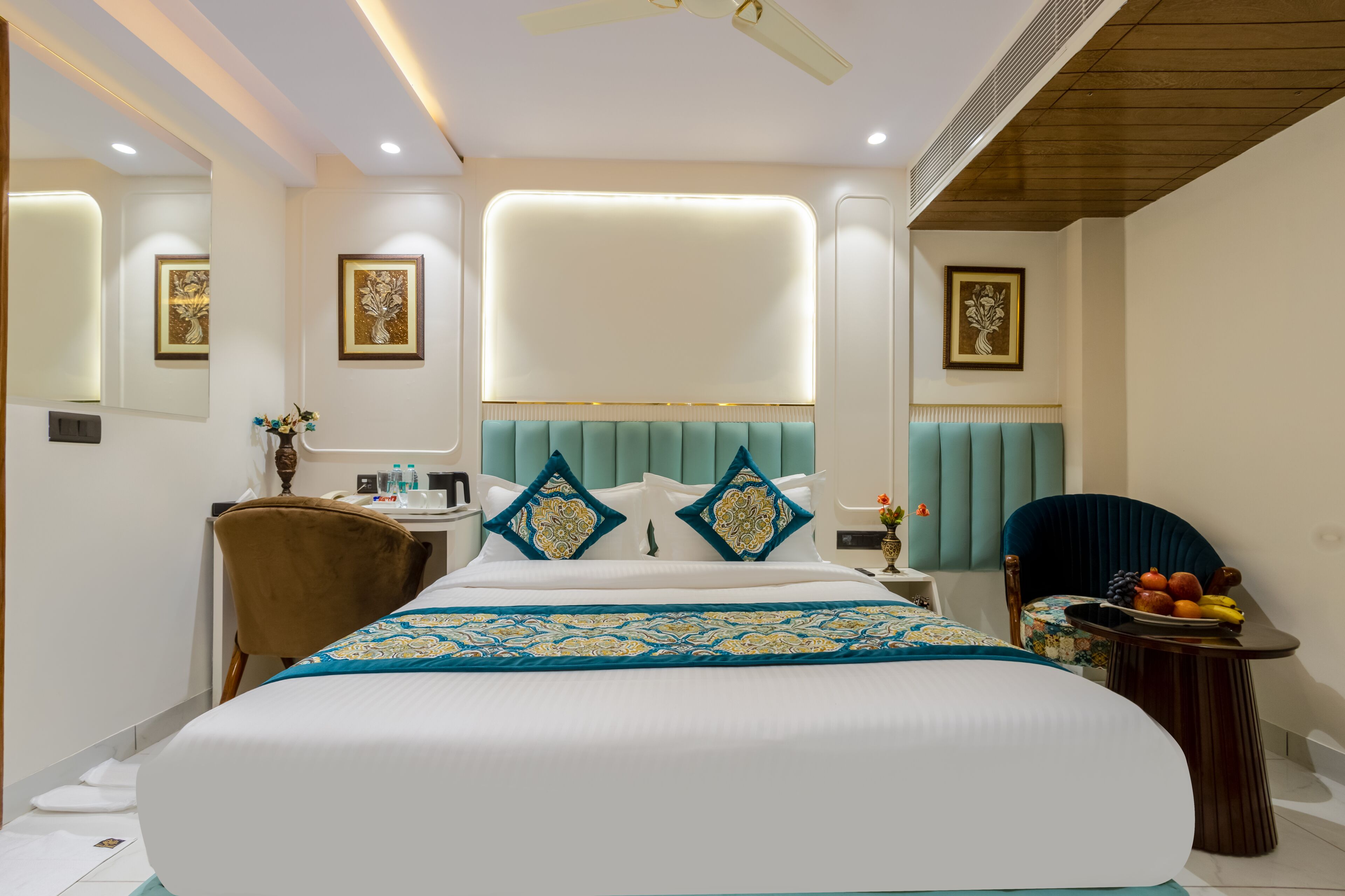 A modern hotel room with a large bed, a desk, a chair, and a small table with fruit.