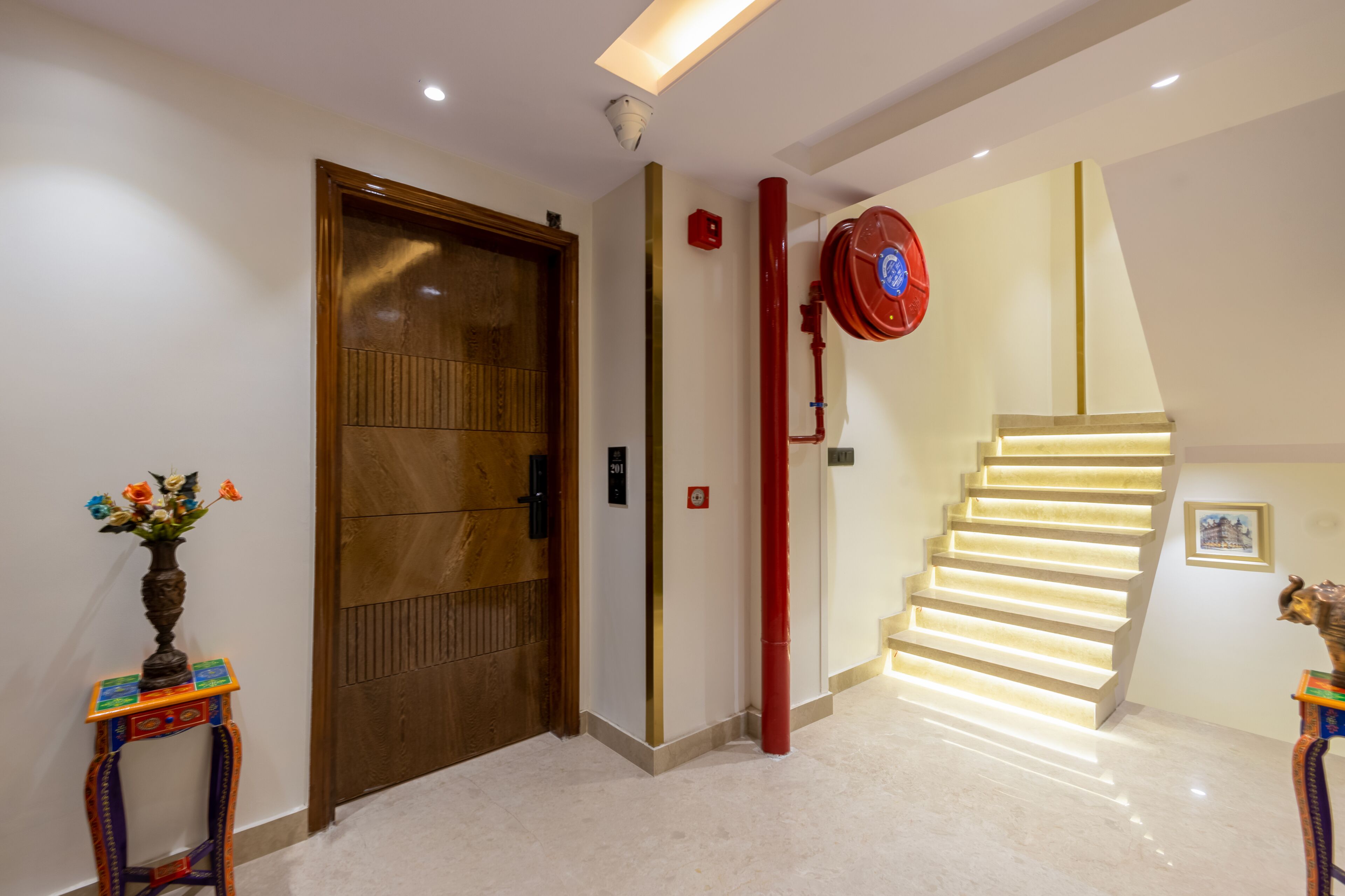 A modern interior with a wooden door, a staircase with illuminated steps, and a wall-mounted fire alarm.