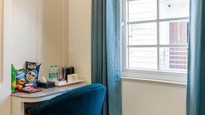 Een kamer met een bureau, een stoel, een schaal fruit, een raam met gordijnen en uitzicht op het buiten.