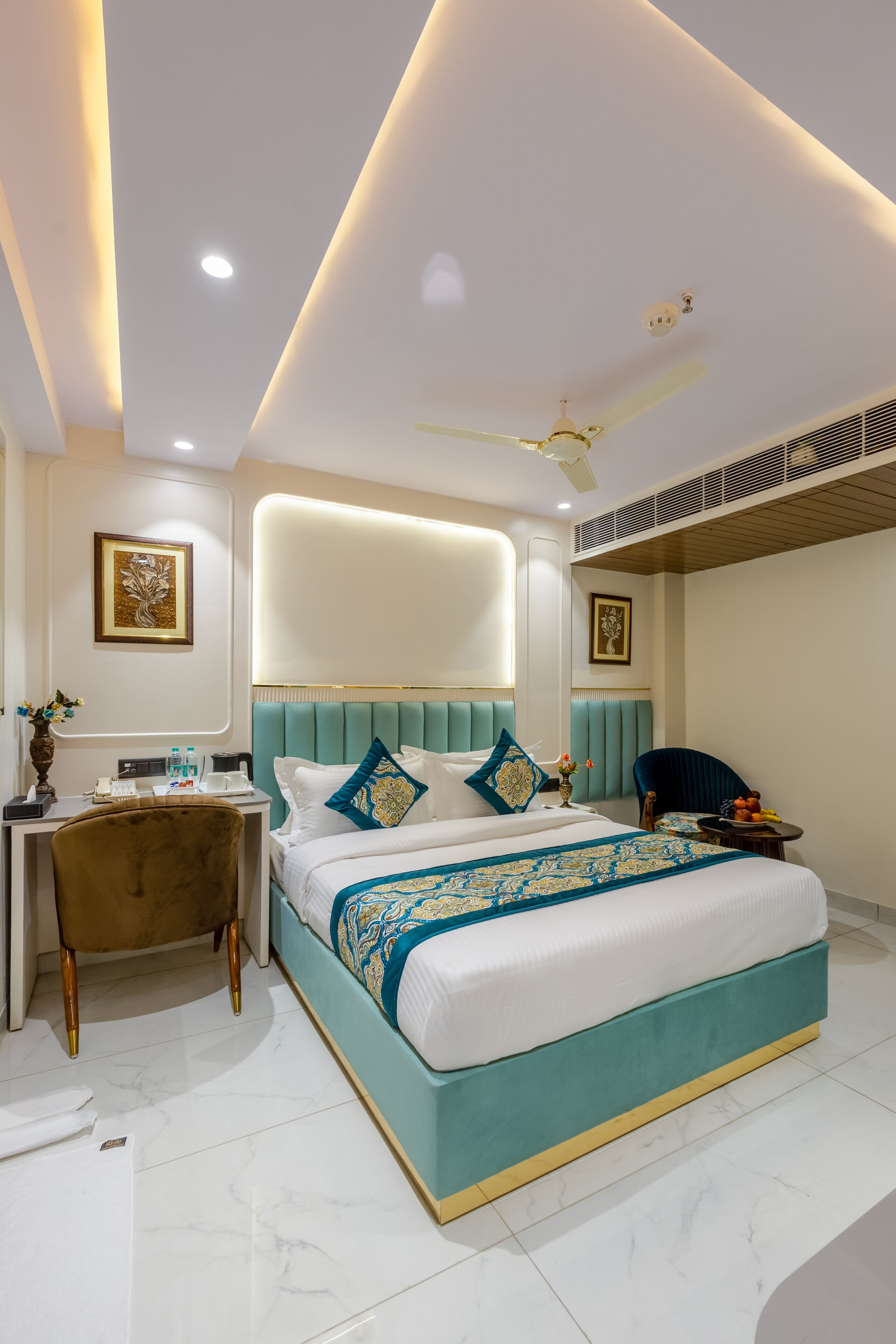 A modern hotel room with a large bed, a desk, a chair, and a ceiling fan.