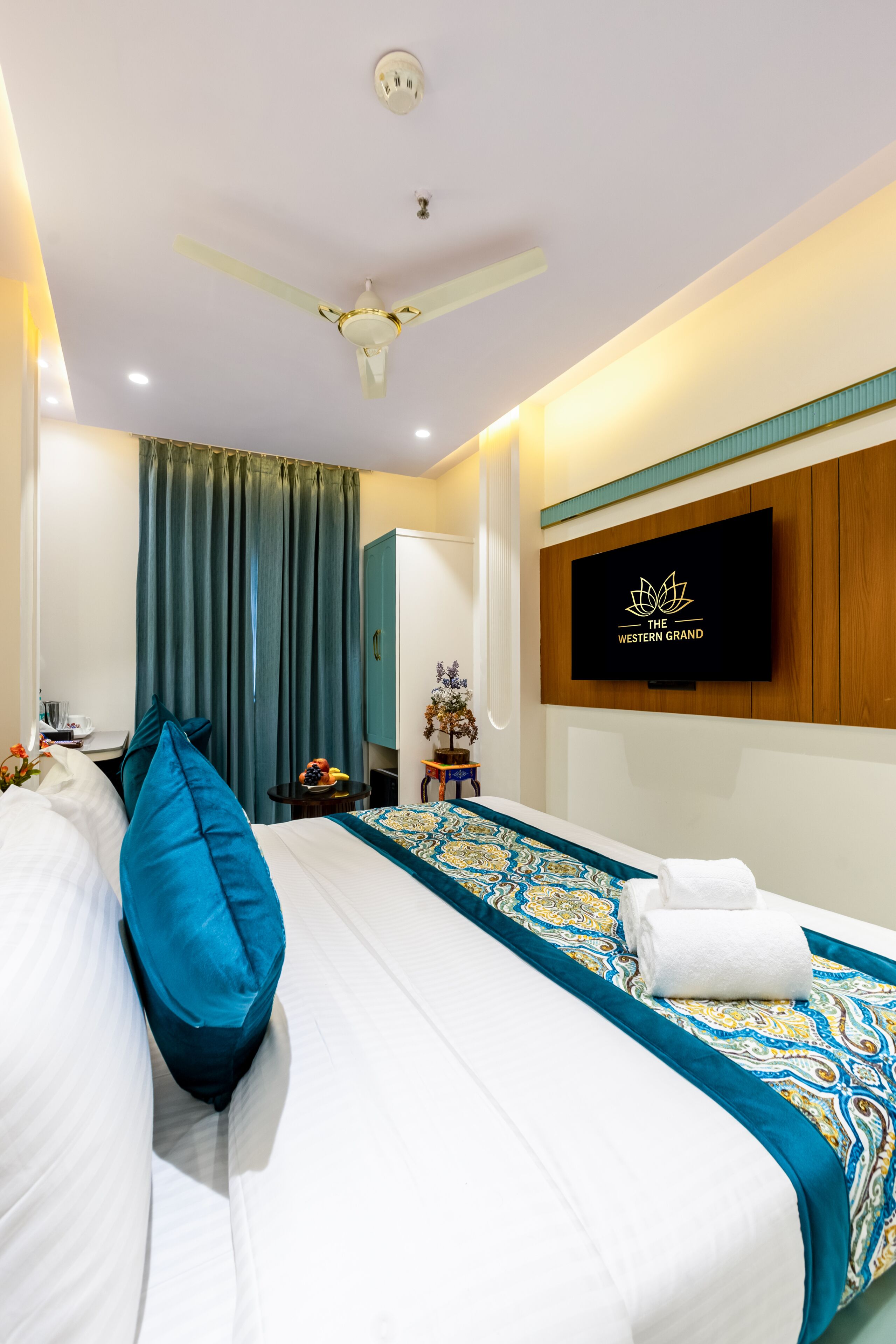 A hotel room with a bed, a ceiling fan, a TV mounted on the wall, and a window with curtains.