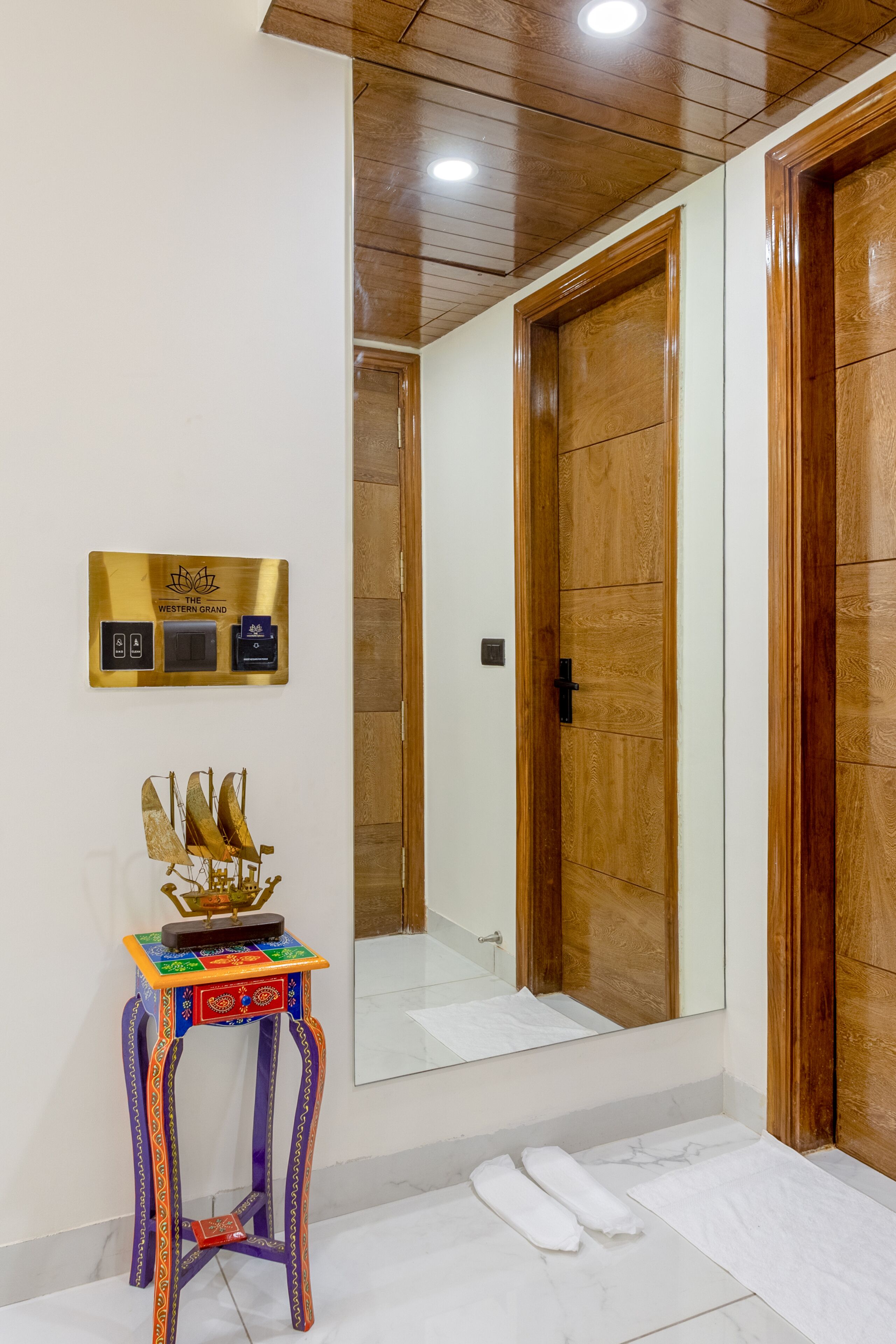 Een badkamer met een houten deur, een spiegel, een klein tafeltje met een decoratieve accessoire, en een bordje met informatie over de voorzieningen.