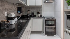 Uma cozinha moderna com armários brancos, bancada preta, forno embutido e exaustor de aço inoxidável.