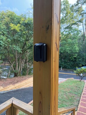 A wooden post with a black object attached to it, surrounded by greenery and a paved area.