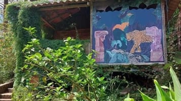A small, rustic hut with a mural of a leopard and a bird, surrounded by lush greenery and trees.