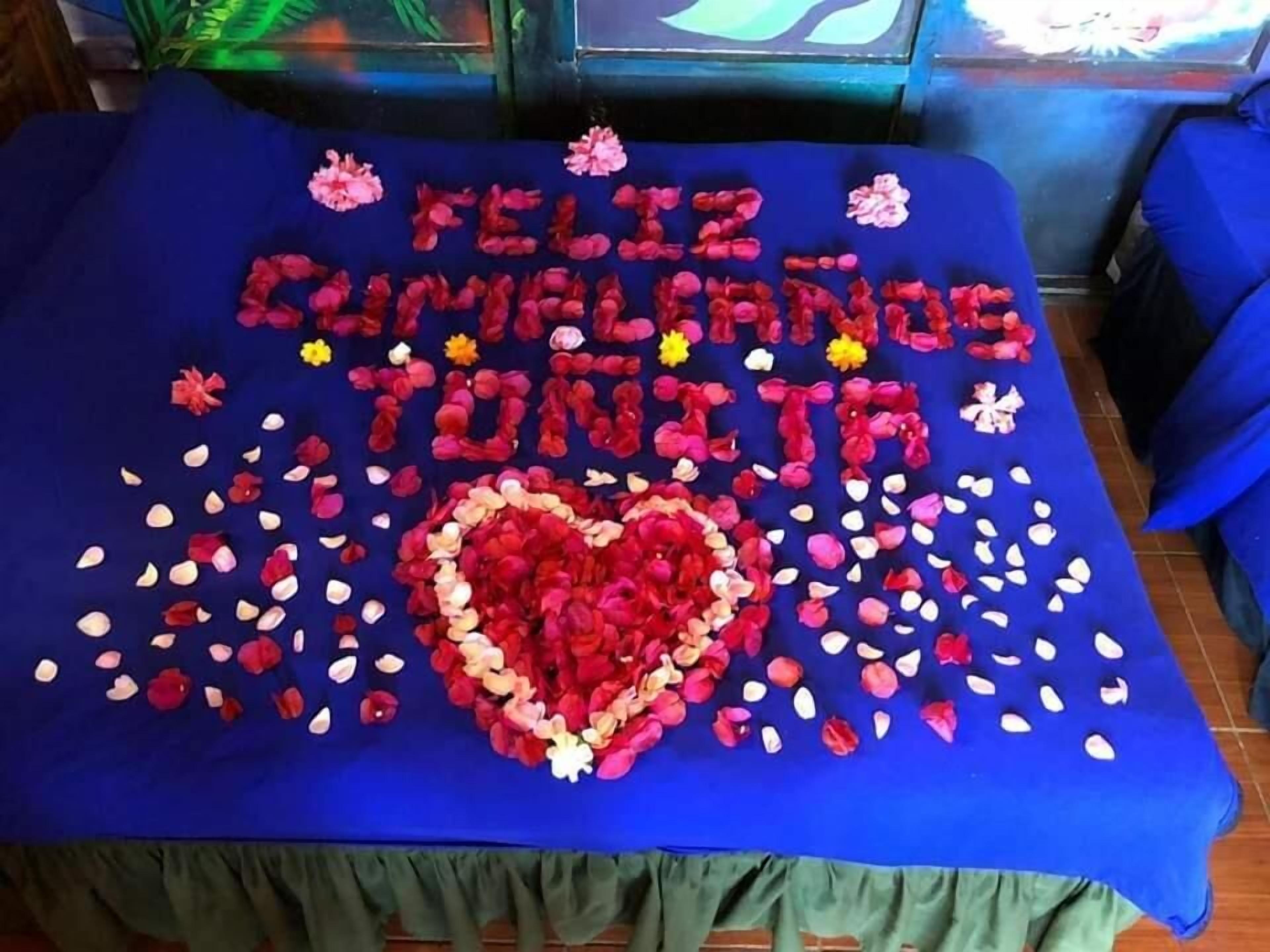 A table with a blue tablecloth, decorated with red and white rose petals and a heart-shaped arrangement of roses.