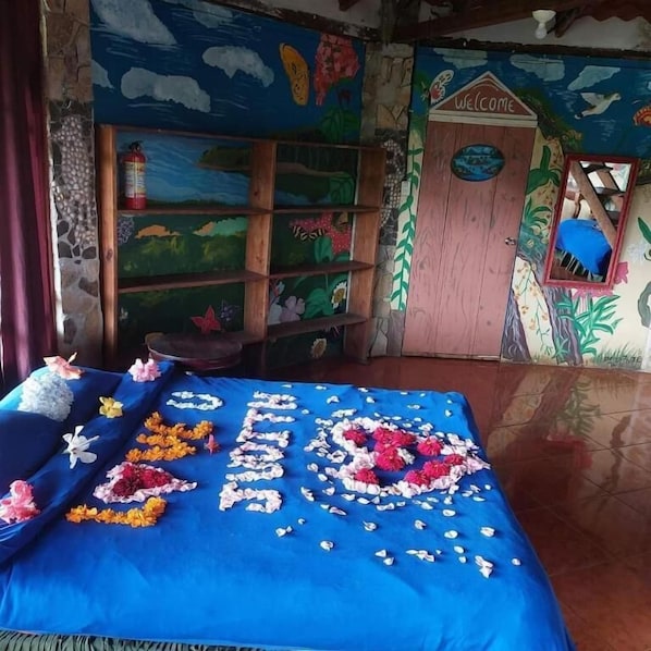 A room with a bed adorned with floral arrangements, a bookshelf, a welcome sign, and a window with a view. - Finca Neblina del Bosque (Esteli)