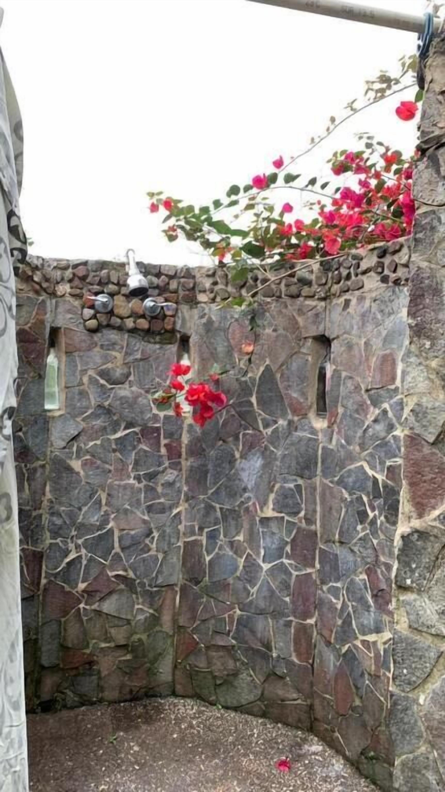 A stone wall with a small opening, a hanging metal object, and red flowers.