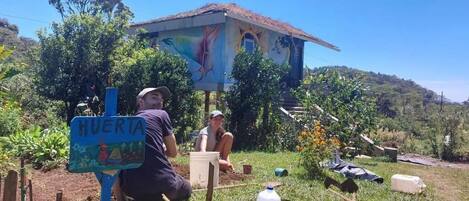 Edificio rústico con un mural, un letrero que dice 'HUERTA' y una persona sentada en una silla.