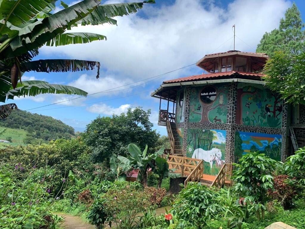 A rustic building with a balcony, surrounded by lush greenery and a painted mural.