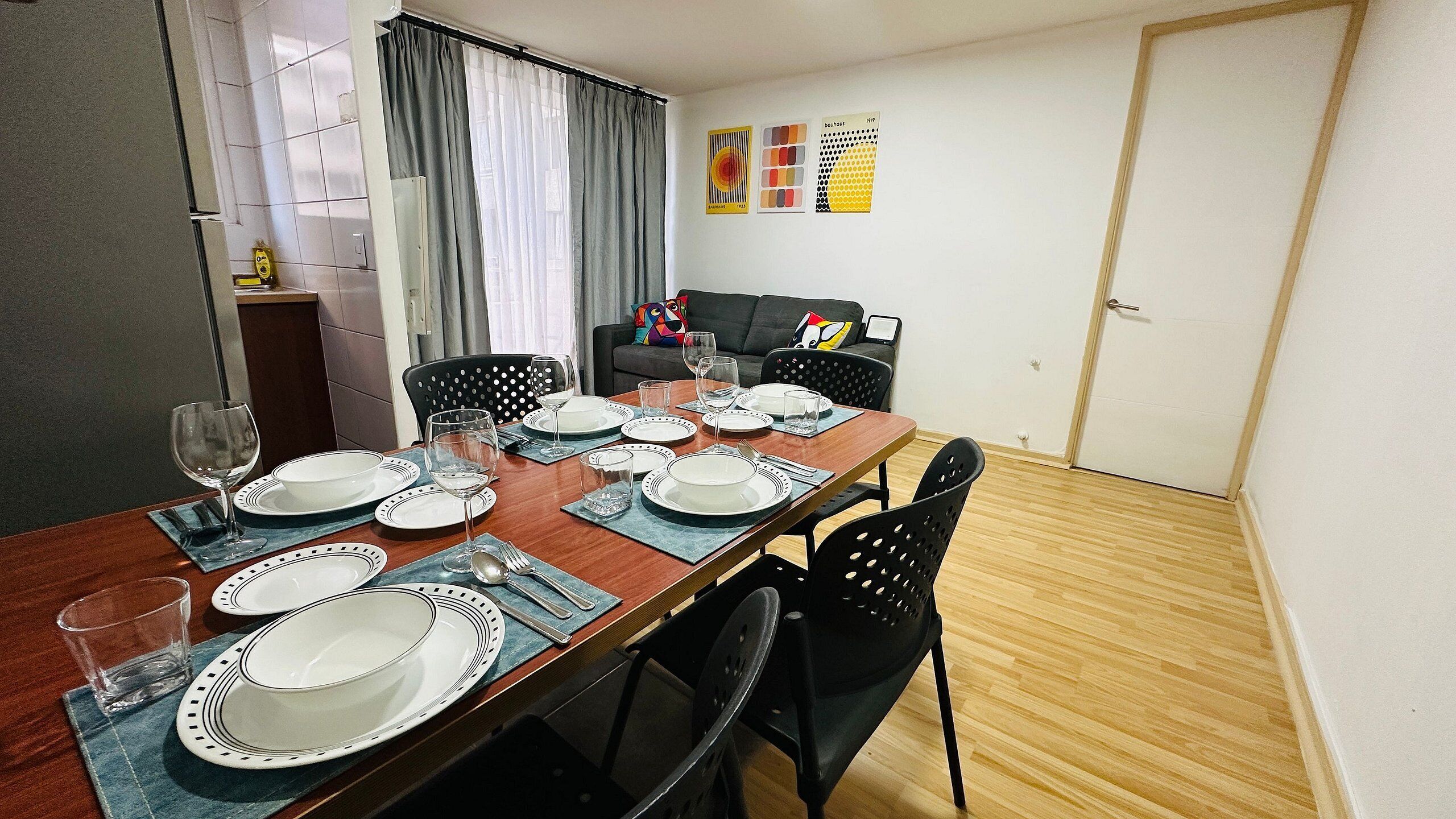 A dining area with a wooden table set for four, chairs, and a sofa in the background.