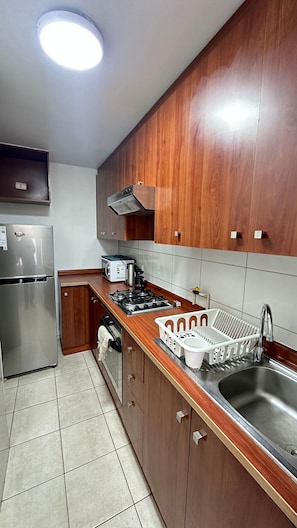 Una cocina con armarios de madera, un refrigerador de acero inoxidable, una estufa a gas y un lavamanos.