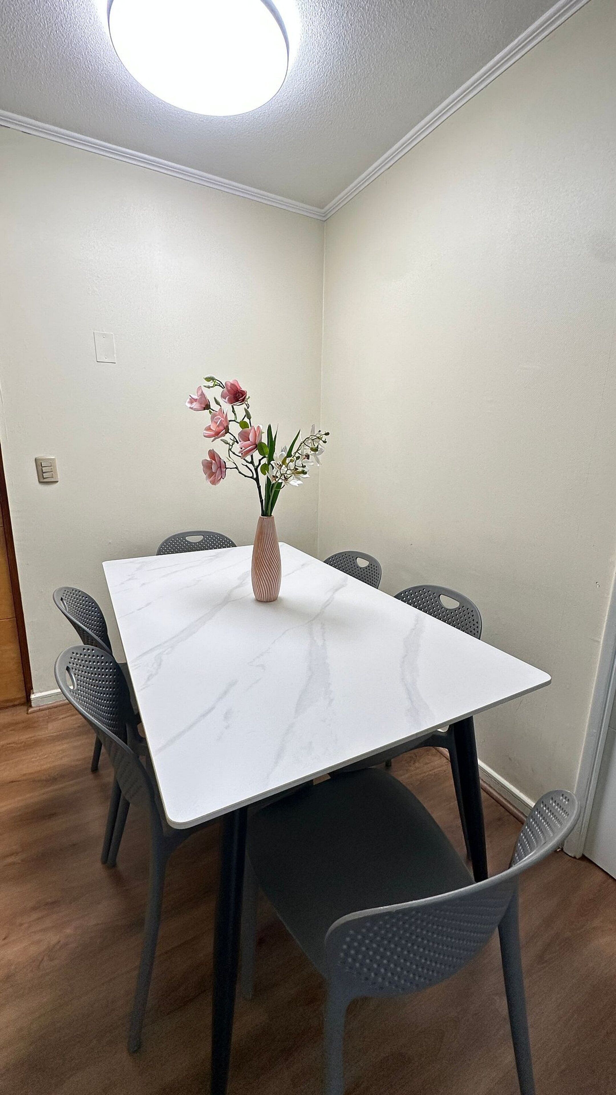 A conference room with a white marble table, six gray chairs, and a vase with flowers.