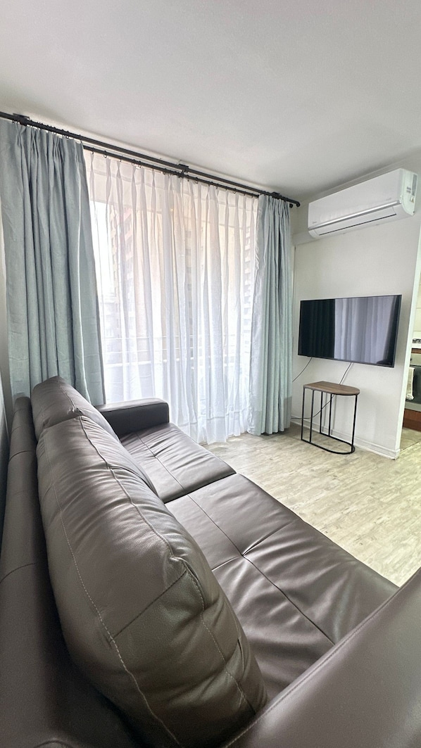 Una sala de estar con sofá, televisor montado en la pared y ventana con cortinas.