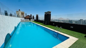 Una piscina en la azotea con vistas despejadas del paisaje urbano y montañas al fondo.