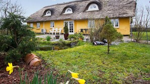 Ein traditionelles Haus mit einem Strohdach, einer gelben Fassade und einem kleinen Garten mit Blumentöpfen und einem Teich.