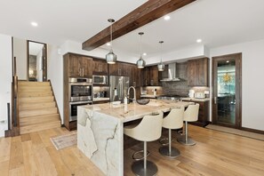 A modern kitchen with a central island, stainless steel appliances, and a wooden staircase. - Charming 5-Bedroom Home w/ Private Spa and A/C in Beautiful West Vail (Vail)