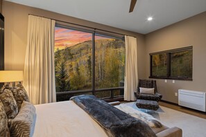 A bedroom with a large window, a bed, a chair, a lamp, and a painting. - Charming 5-Bedroom Home w/ Private Spa and A/C in Beautiful West Vail (Vail)