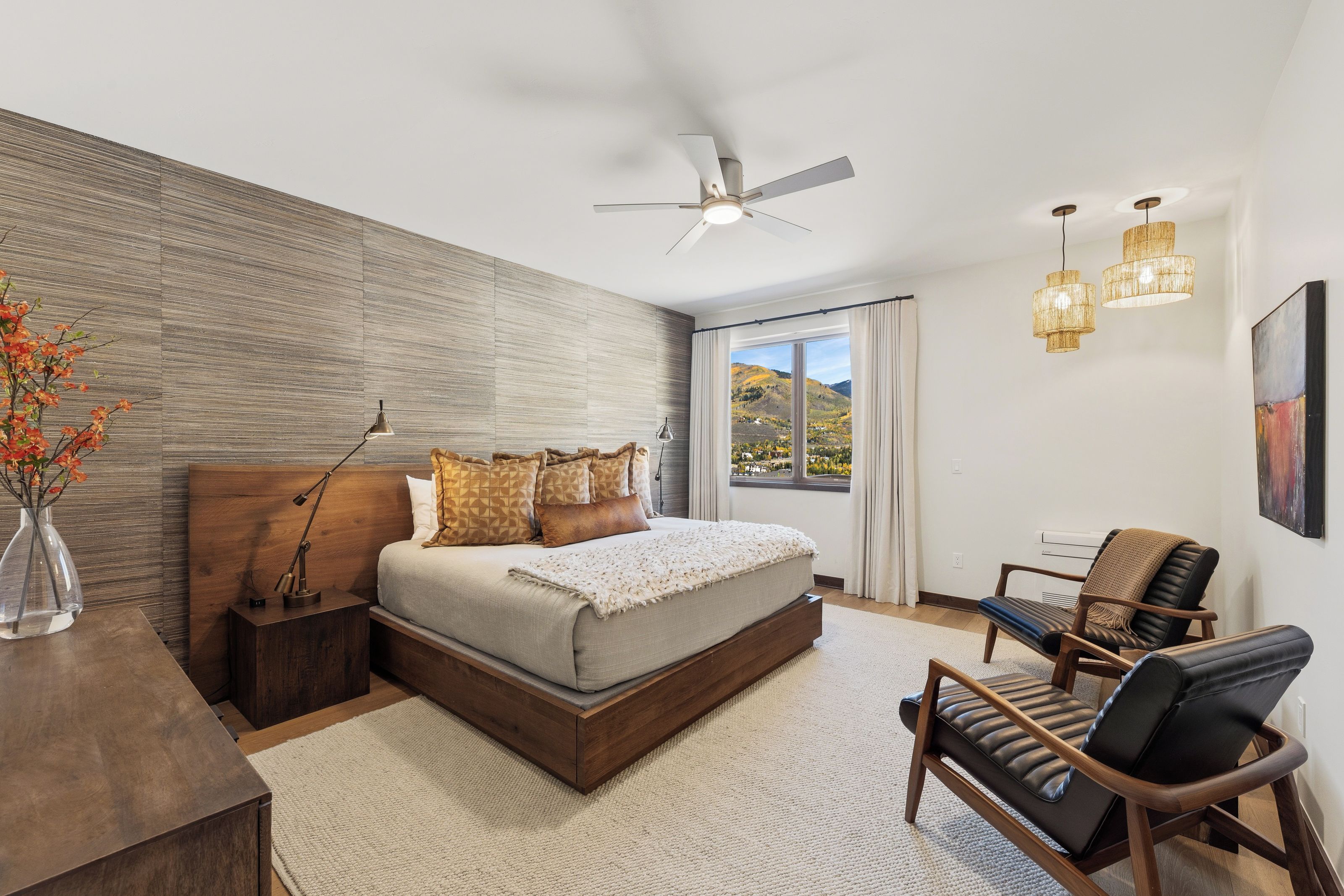 Un dormitorio con cama, escritorio, silla, ventilador de techo y ventana con vistas al exterior.
