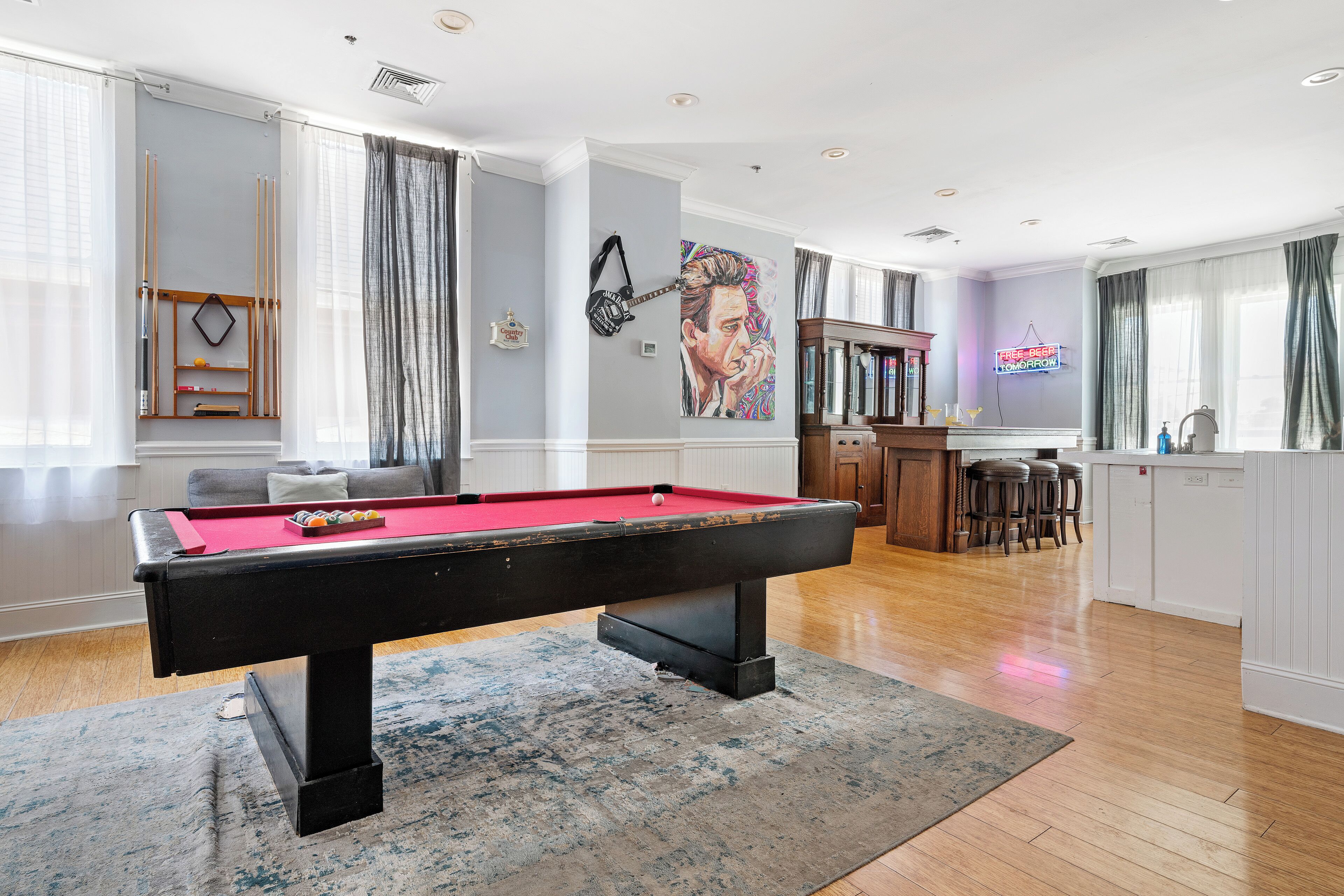 A pool table in a room with a bar area, a painting on the wall, and a view of the kitchen.