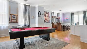 A pool table in a room with a bar area, a painting on the wall, and a view of the kitchen.