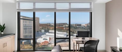 A modern living room with a large window, a sofa, a dining table, and a chair.
