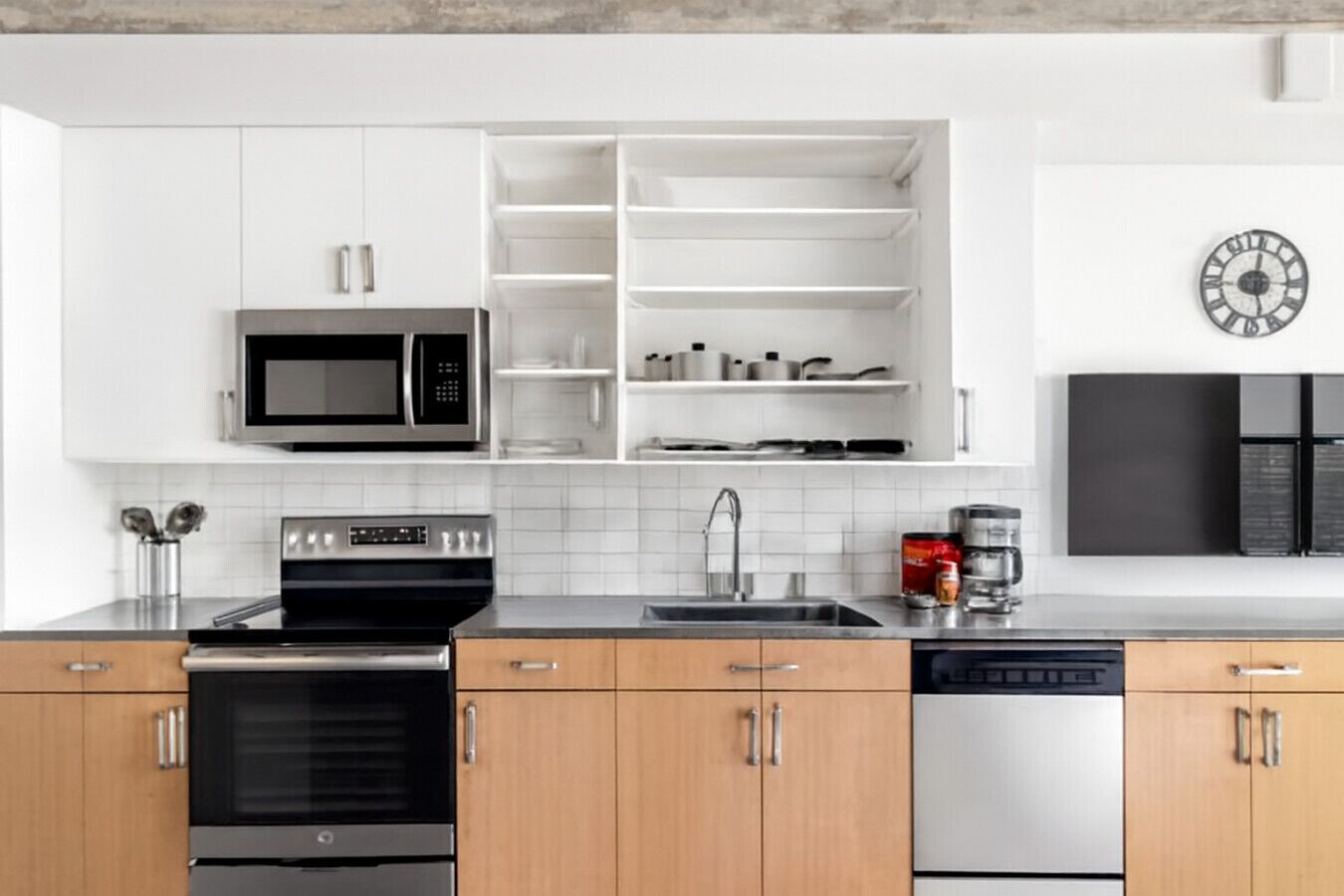A modern kitchen with white cabinets, a stainless steel microwave, an oven, a dishwasher, and a coffee maker.