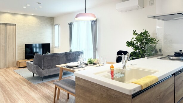 A modern kitchen with a central island, a dining area with a sofa and table, and a living room with a TV and seating. - Akikawa Waifu 2 | 25 min to TSMC | Entire 4LDK House | Up to 8 Guests (菊池市)