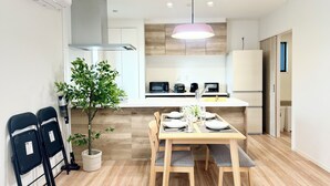 A modern kitchen with a dining table set for four, a potted plant, and a ceiling light fixture. - Akikawa Waifu 2 | 25 min to TSMC | Entire 4LDK House | Up to 8 Guests (菊池市)