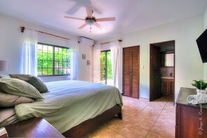 Ein Schlafzimmer mit einem Bett, Vorhängen, einem Deckenventilator und Blick ins Freie.